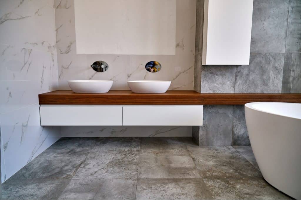 photo of a Luxury bathroom vanity. Ceramic round sinks placed on teak tabletop in luxury bathroom with gray and white marble walls