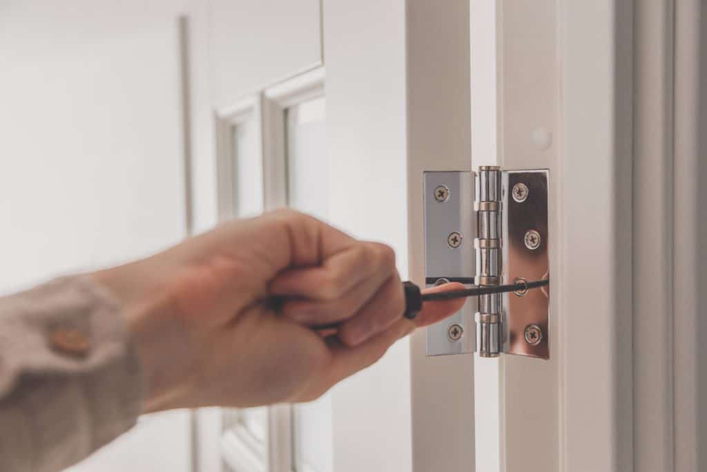 photo of man using a screwdriver to remove hinges from door