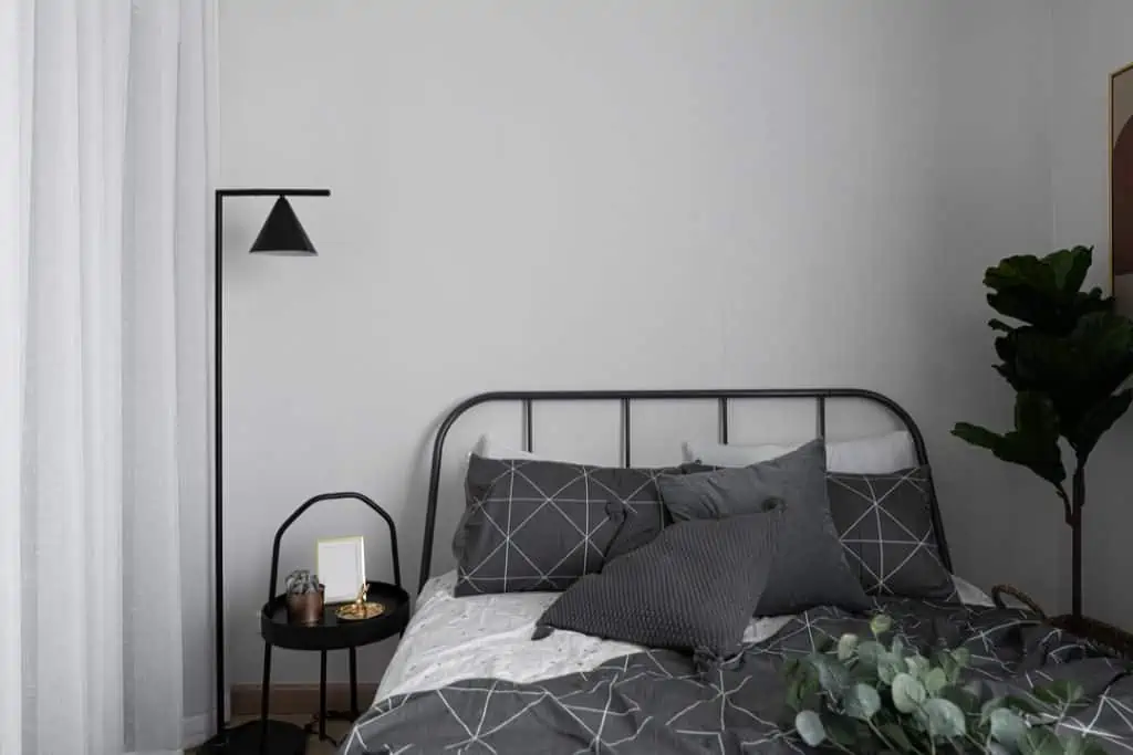 Bedroom corner in scandinavian style with gray metal bed and black side table with minimal floor lamp